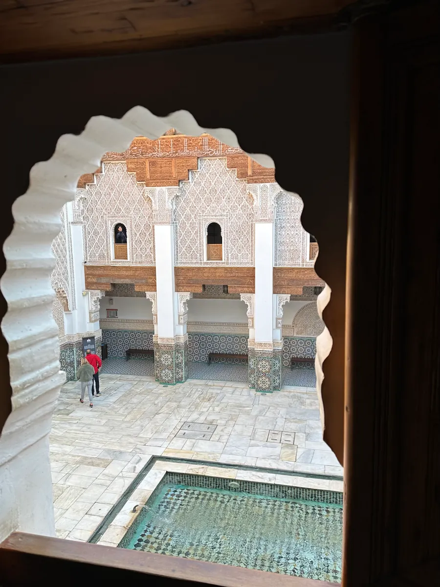 Cour de la médersa Ben Youssef à Marrakech vue à travers un arc en stuc ciselé, bassin et zellige